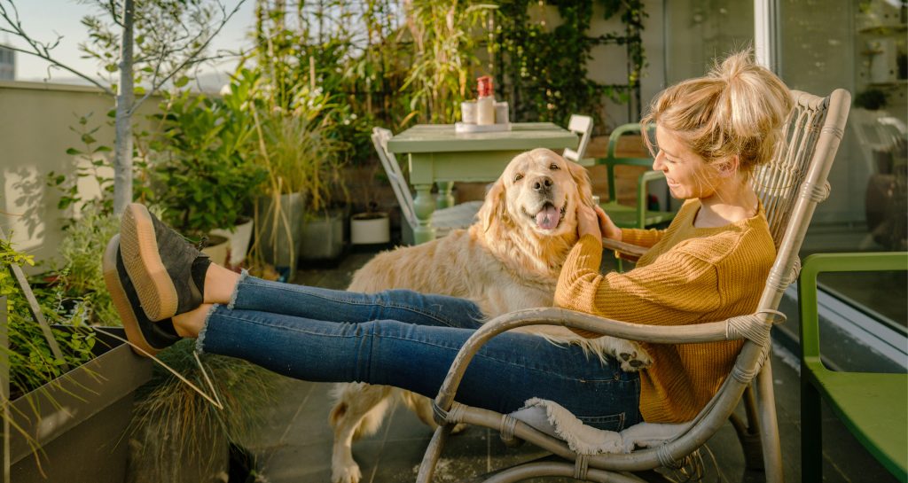 Kvinne og hund slapper av på blomstrete balkong med sitt grønne boliglån fra Sparebanken Øst.