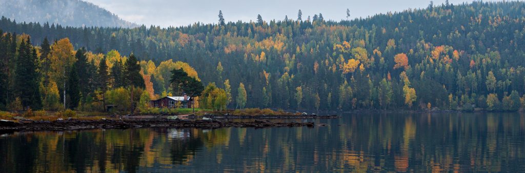 Hytte plassert med et stort vann omringet av skog i høstens farger.