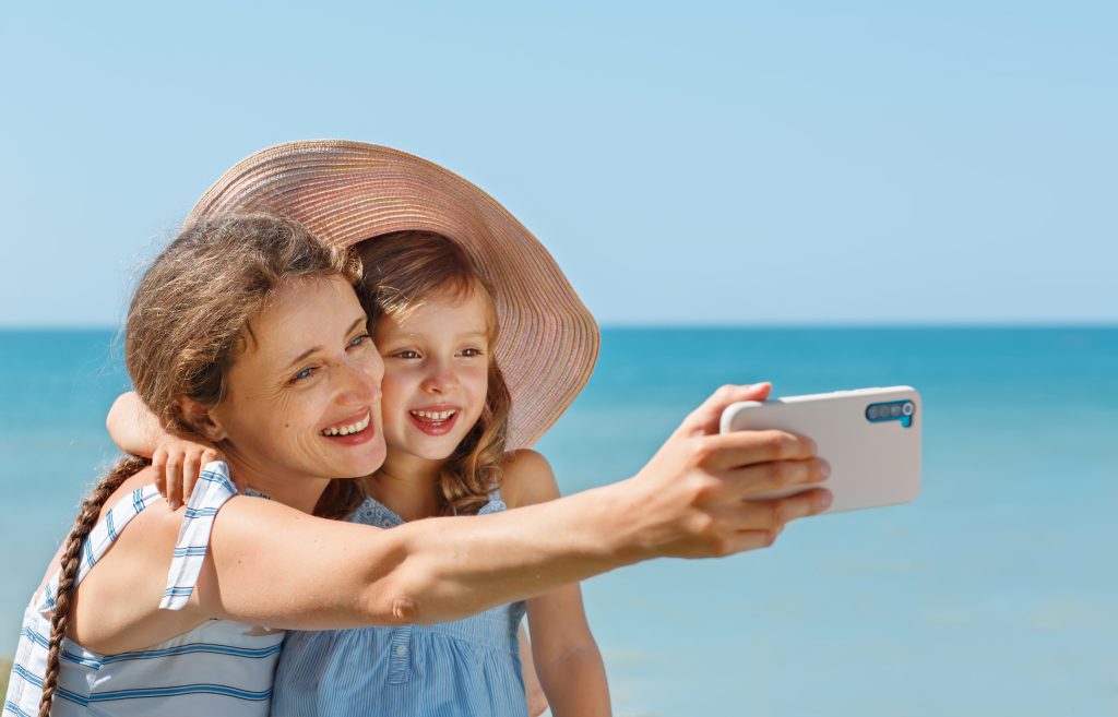 Mor og barn på stranden med mobil - reiseforsikring